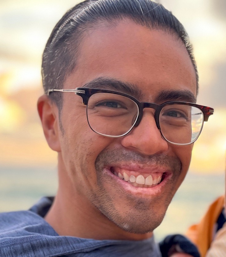 Headshot of Allistair Mallillin. Allistair is wearing black framed glasses and a blue shirt.