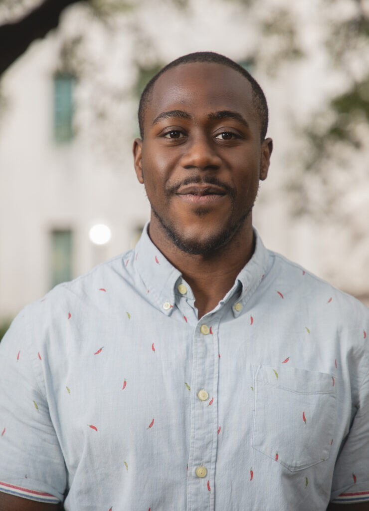 Headshot for Chimene Okere. Chimene hears a light blue button-up with red and green embroidered chilis.